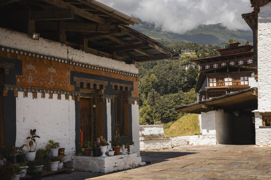 View of traditional Bhutanese architecture with ornate white walls, dark window frames, and vibrant orange detailing against a backdrop of misty mountains, Trongsa, Bhutan. - Powered by Adobe