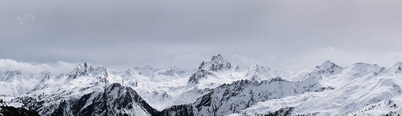 Obraz premium Expansive panoramic view of a snow-covered alpine mountain range under moody winter clouds in the European Alps