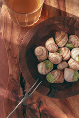 Snails cooked with herb oil on a wooden plate, served with white wine, natural light, no people,