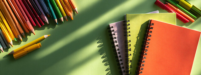 Vibrant colored pencils and stacked spiral notebooks on a green desk, top view