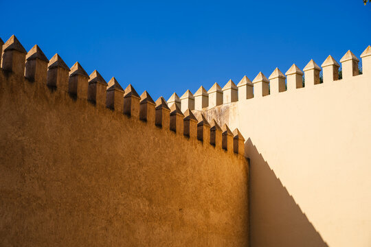 Sunlit stone walls with triangular crenellations against a clear blue sky. Fez, Fez-Meknes, Northern Inland Morocco