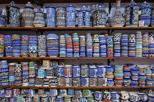 Colorful ceramic mugs and jugs organized on wooden shelves in a vibrant display. Fez, Fez-Meknes, Northern Inland Morocco