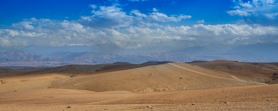Vast desert landscape with rolling hills under a bright blue sky with scattered clouds. Agafay Desert, Marrakesh-Safi, Morocco