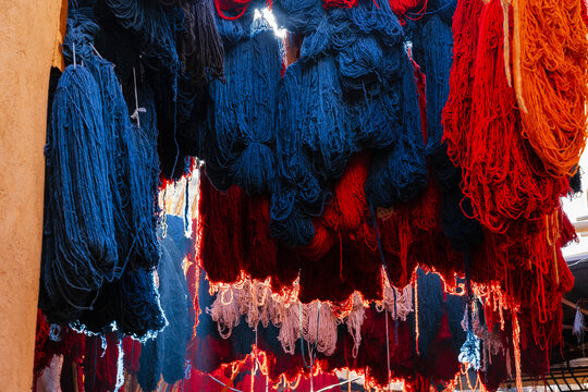 Colorful yarn bundles hang in an open market, illuminated by sunlight from above. Marrakesh, Morocco