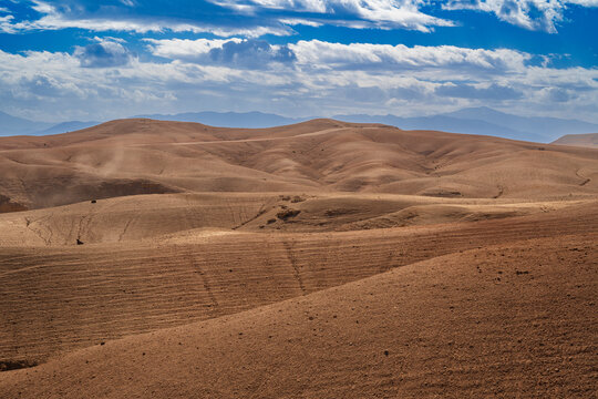 Rolling desert hills under a partly cloudy blue sky with distant mountains in view. Agafay Desert, Marrakesh-Safi, Morocco
