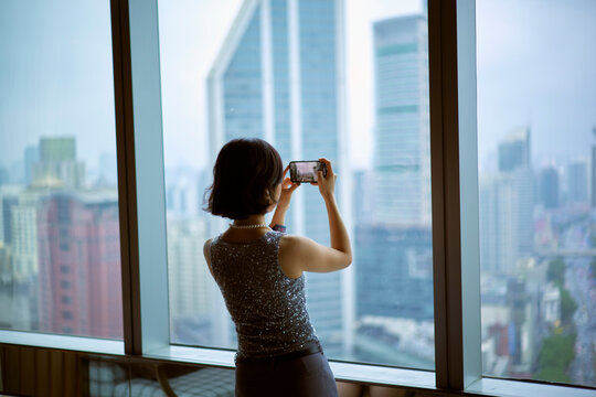 Woman photographing a city skyline through large window in a high-rise building. Shanghai, China
