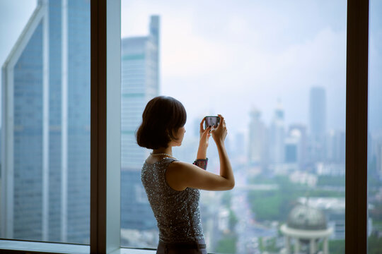 Woman taking a photo of a city skyline from a high vantage point near a window. Shanghai, China