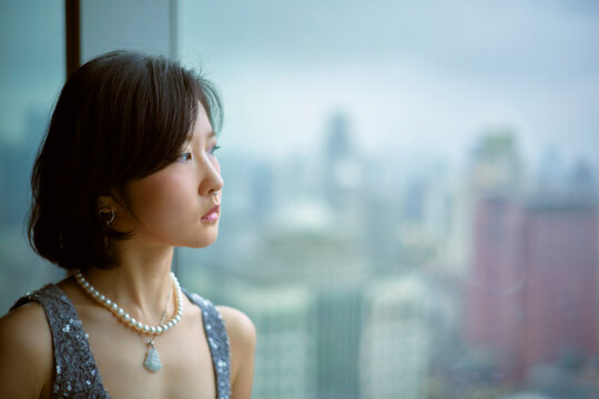 Woman in a pearl necklace gazing out a window with a city skyline in the background. Shanghai, China