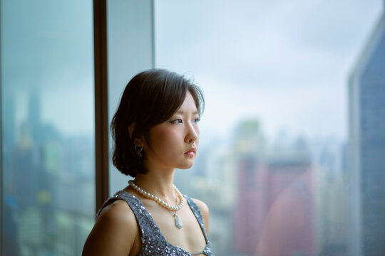 Woman in elegant dress looks out at city skyline through large window. Shanghai, China