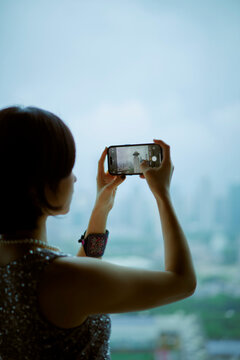 Woman taking a photo of a city skyline with a smartphone from a high vantage point Shanghai, China 
