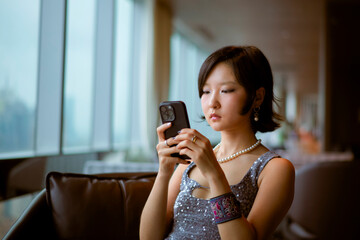 Woman in elegant attire focused on her phone in a modern, softly lit interior. Shanghai, China 