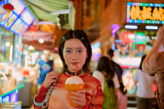 Young woman in vibrant market drinking bubble tea under colorful neon lights at night. Shanghai, China
