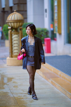 Woman in black jacket and skirt walking on wet sidewalk holding pink bag. Shanghai, China 