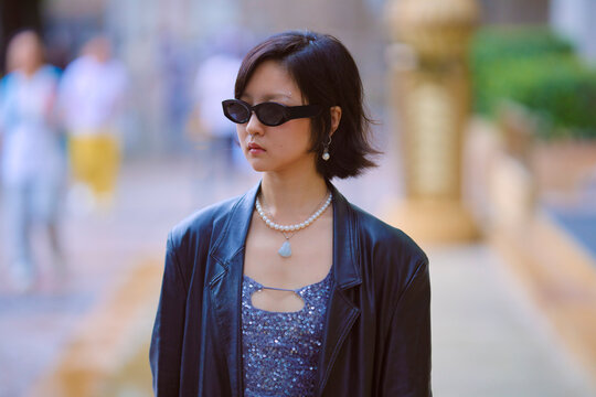 Woman in sunglasses walks outdoors wearing a leather jacket and beaded necklace. Shanghai, China
