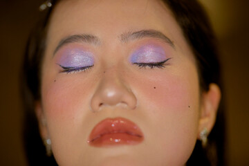 Woman with pink and purple eye makeup and glossy lips with eyes closed in close-up view. Shanghai, China