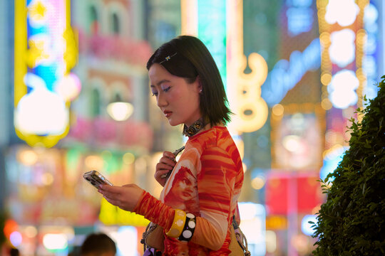 Young woman reading her phone in a colorful, vibrant cityscape at night. Shanghai, China
