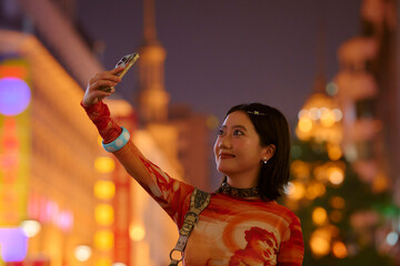Young woman taking a selfie against a vibrant, colorful city backdrop at night. Shanghai, China