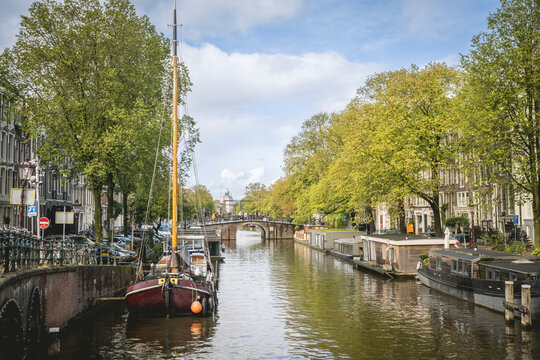 Boats lined along a canal in a charming European city with lush trees and historic buildings. Amsterdam,. Netherlands