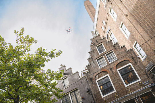 Buildings with traditional architecture under a clear sky as a plane flies over. Amsterdam, Netherlands