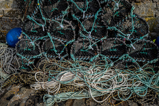 Stacks of lobster pots with tangled ropes and a blue buoy on a rocky surface. Keiss harbour, Scotland