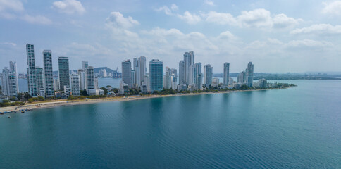 City skyline with tall skyscrapers lining a calm blue waterfront under a cloudy sky. Cartagena, Colombia