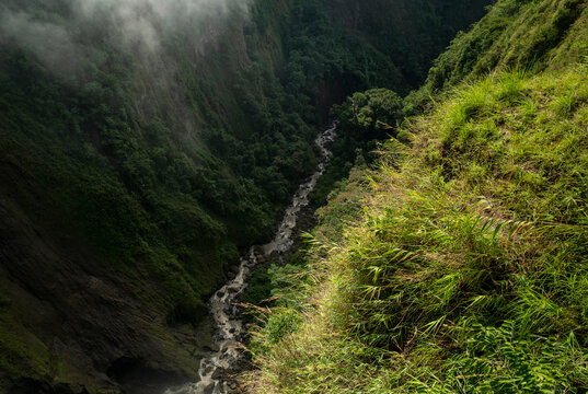 Lush green canyon with a river flowing through, shrouded in mist, in a tropical setting. San Agustin, Colombia