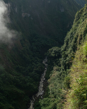 Lush green valley with a narrow river flowing through dense forest and misty cliffs. San Agustin, Colombia