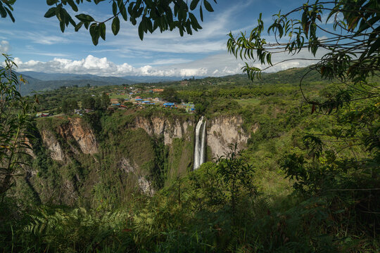 Scenic view of a waterfall cascading into a lush green canyon with a small village nearby. San Agustin, Colombia