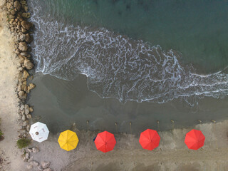 Aerial view of colorful umbrellas lining a rocky beach with waves lapping the shore. Cartagena, Colombia