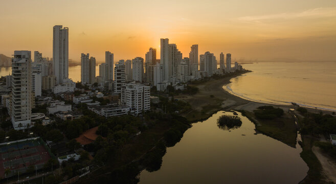 Tall city buildings along a coastal shoreline at sunset with a calm body of water nearby. Cartagena, Colombia