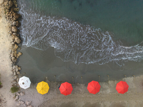Aerial view of colorful umbrellas lining a rocky beach with waves lapping the shore. Cartagena, Colombia