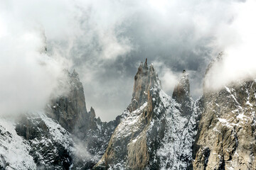 Majestic snow-covered mountain peaks rise through swirling clouds in a dramatic landscape. Valle d'Aosta, Italy