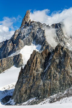 Rugged mountain peaks with snow patches under a bright blue sky with fluffy clouds. Valle d'Aosta, Italy