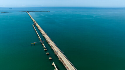 Aerial view of a long industrial pier. The azure and turquoise water of the sea extend to the horizon.