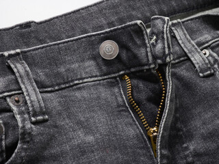 Close-up of black denim jeans with a partially open gold zipper and buttoned waistband.