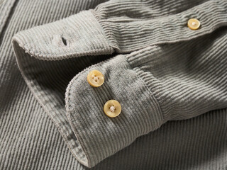Close-up of a grey corduroy fabric shirt with yellow buttons on the sleeve.