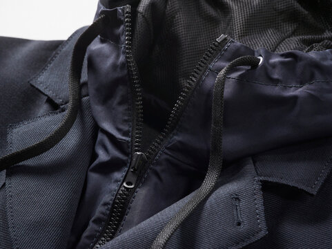 Close-up of a dark blue jacket with a zipper and drawstrings against a light background.