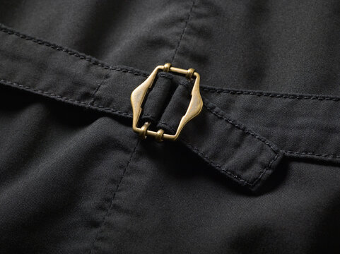 Close-up of a brass buckle on a dark fabric with detailed stitching.