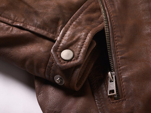 Close-up of a brown leather jacket with a metal zipper and button detail.