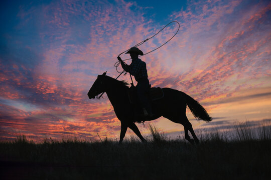 Silhouette of a cowboy on horseback with a lasso against a vibrant sunset sky. Oregon, USA