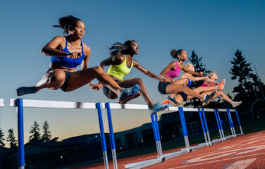 Athletes race over hurdles on a track at dusk, displaying strength and determination. WA, USA
