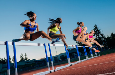 Athletes mid-air hurdling on a track under a clear blue sky during a race. WA, USA