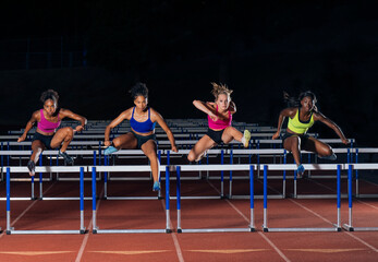Four athletes in vibrant sportswear leap over track hurdles in a synchronized motion. WA, USA