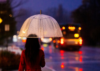 Person with umbrella standing in the rain at night near bus with colorful city lights. WA, USA