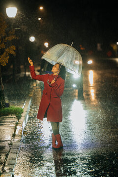 Woman in red coat with umbrella on rainy street at night, lit by streetlights. WA, USA