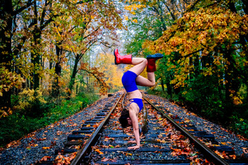 Woman in blue athletic wear does a handstand on railroad tracks surrounded by autumn trees. WA, USA