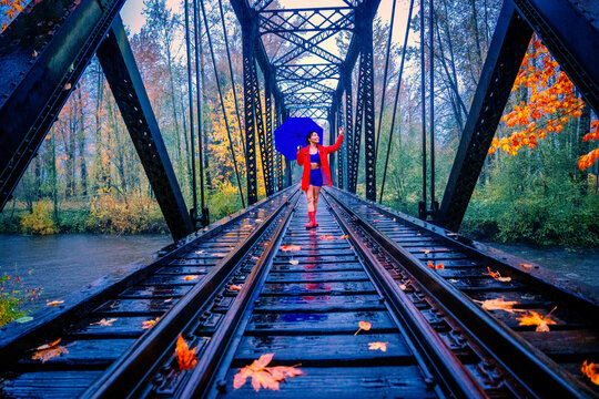 Woman with blue umbrella walking on a railway bridge surrounded by autumn foliage. WA, USA