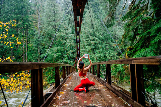 Woman in red outfit kneeling on a wooden bridge holding a glass orb surrounded by lush greenery. WA, USA