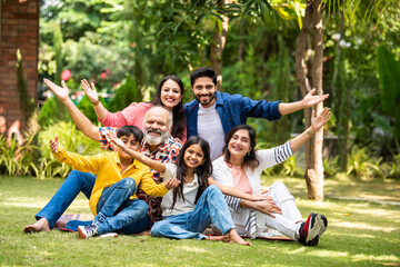 Indian family of three generations smiling and bonding outdoors on green park lawns