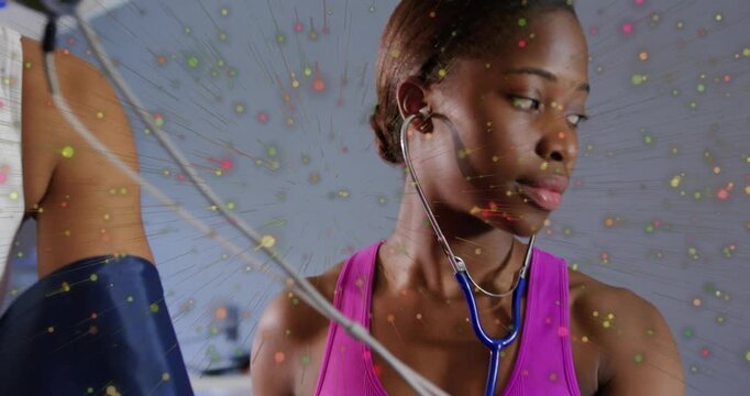 Trainer in pink tank placing cuff, taking BP, watching gauge amid speckle overlay for health